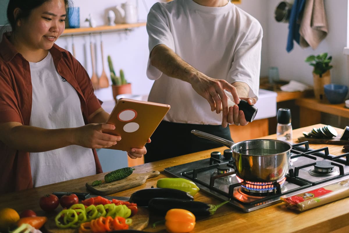 Two people cooking together and checking a recipe on a tablet