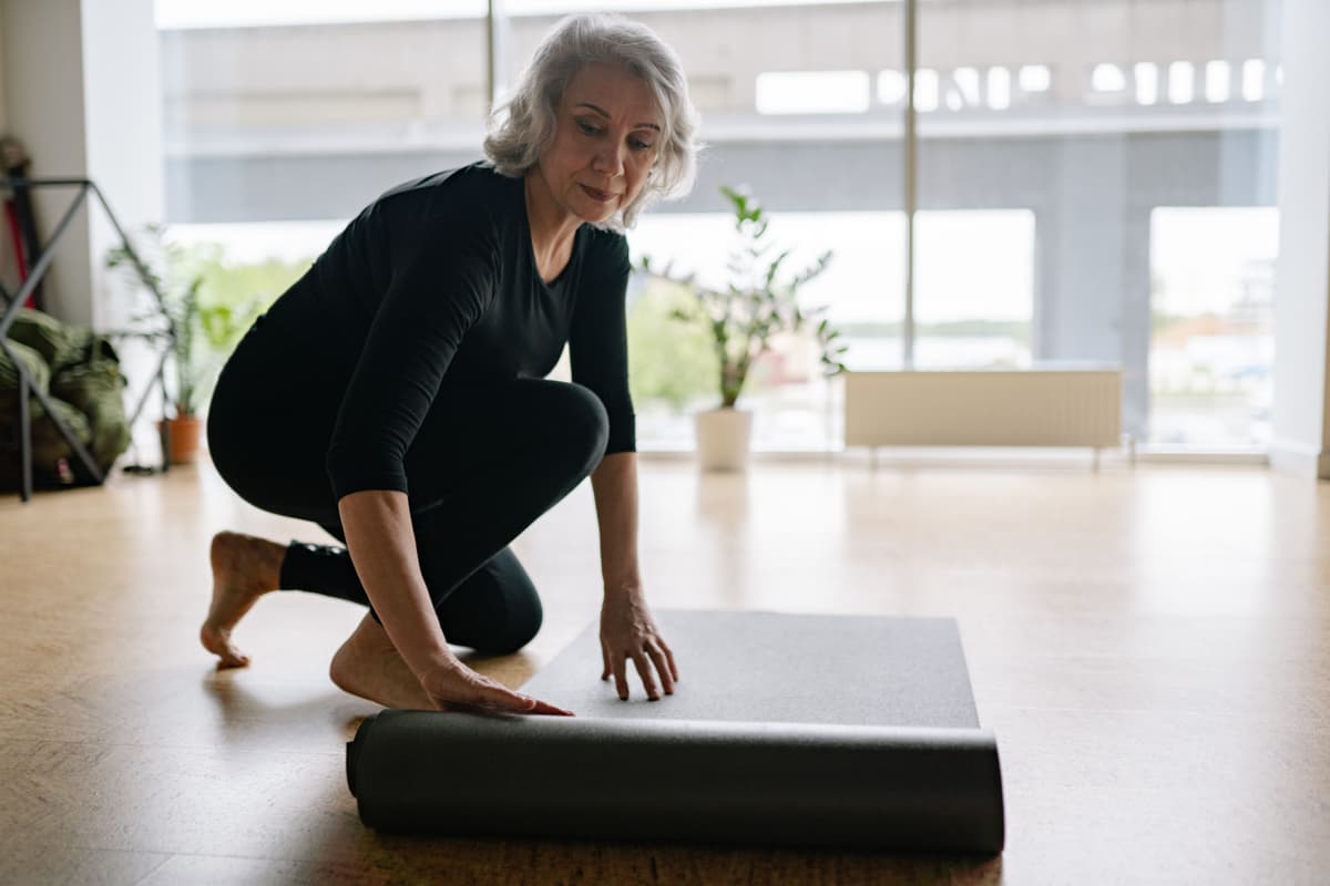 An older woman rolling out an exercise mat at home
