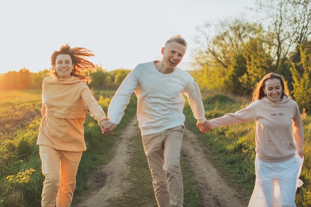 Friends running hand in hand along a country track at sunset