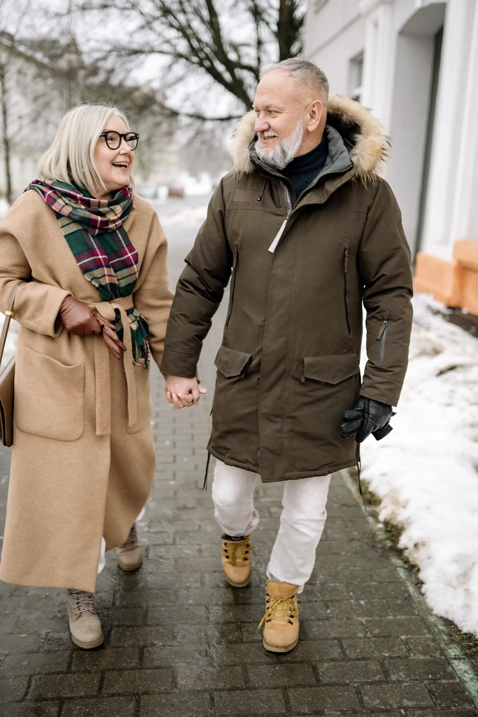 An older couple walking hand in hand on a snowy pavement